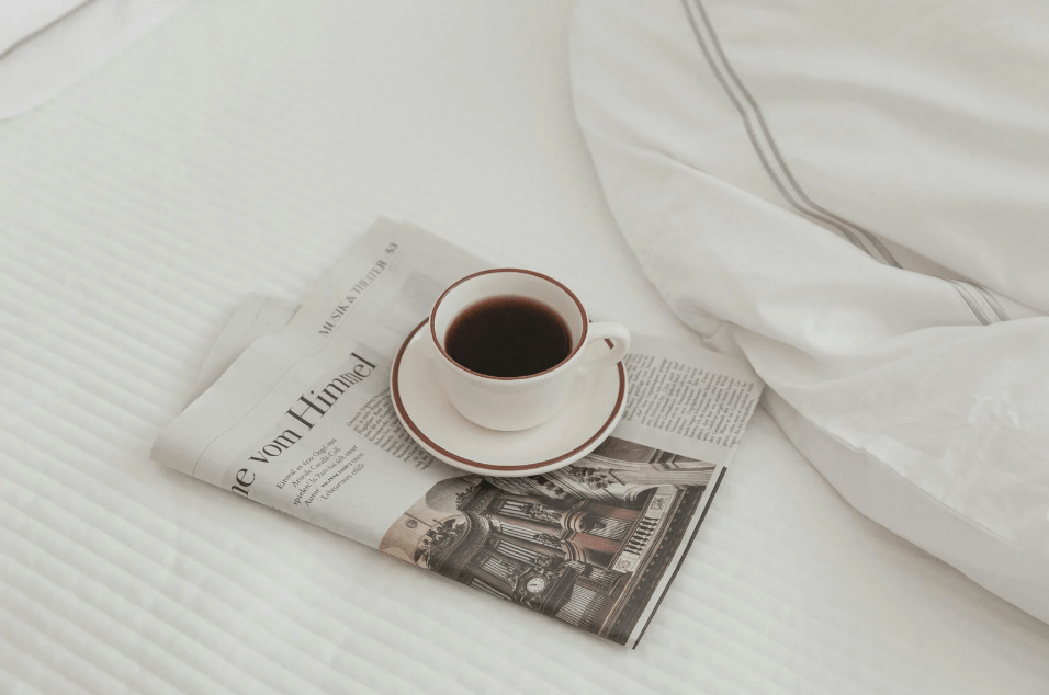 Una taza de café sobre un periódico en una cama.