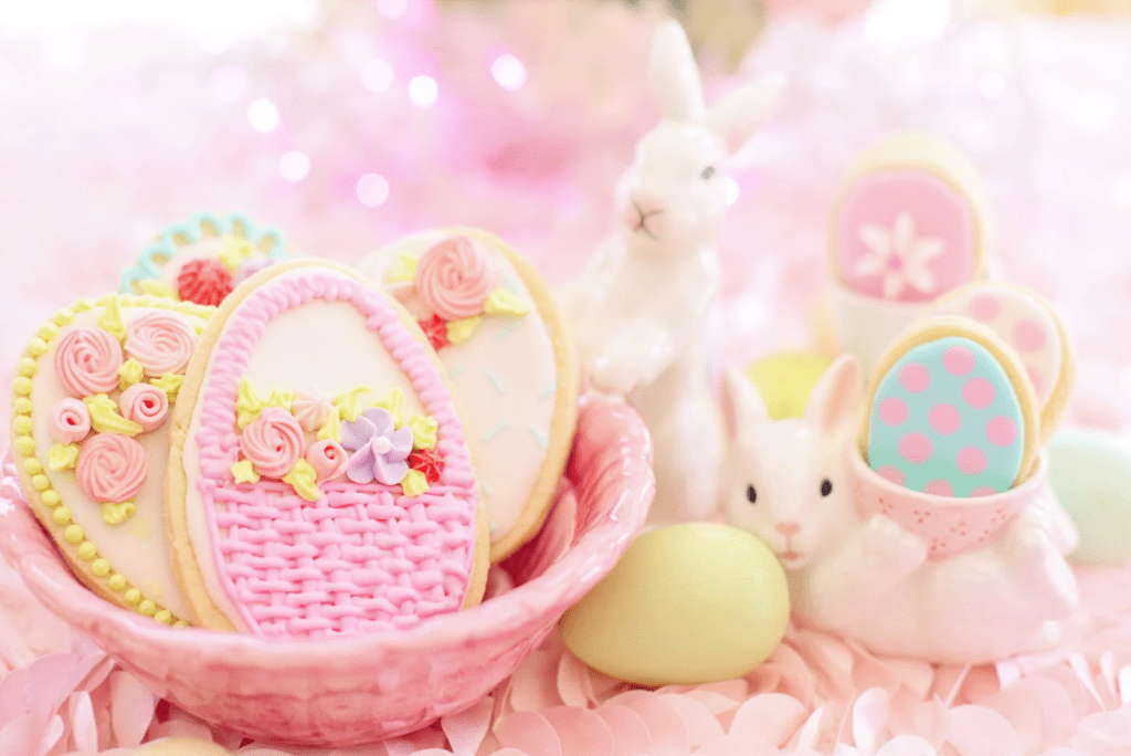 Una cesta con galletas decoradas con dibujos de pascua, y dos figuras de conejitos junto a ella.