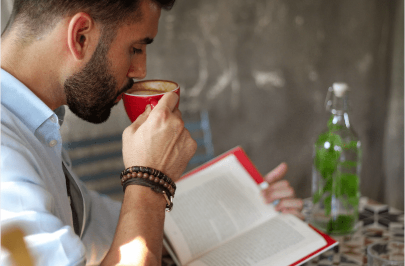 Un joven lee mientras bebe café.