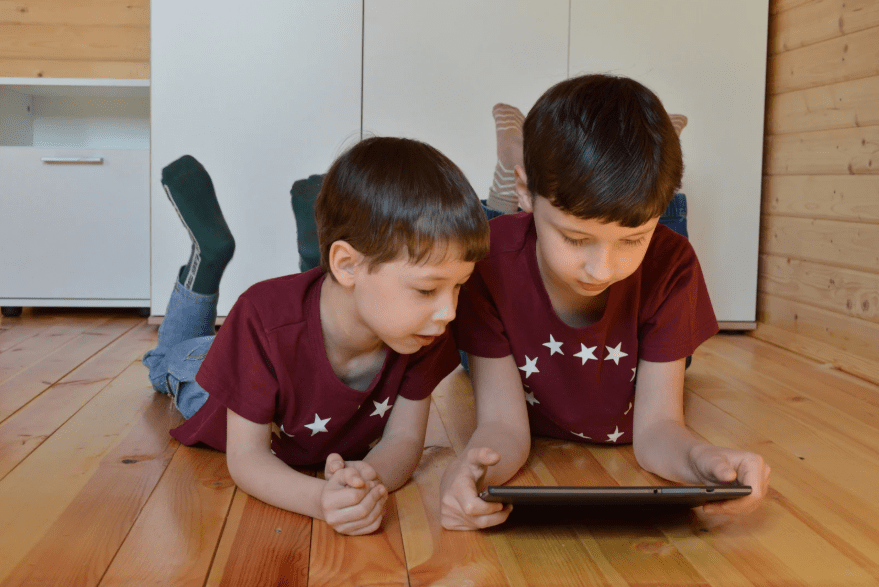 Dos niños tumbados n el suelo, vestidos igual, y mirando una tablet.
