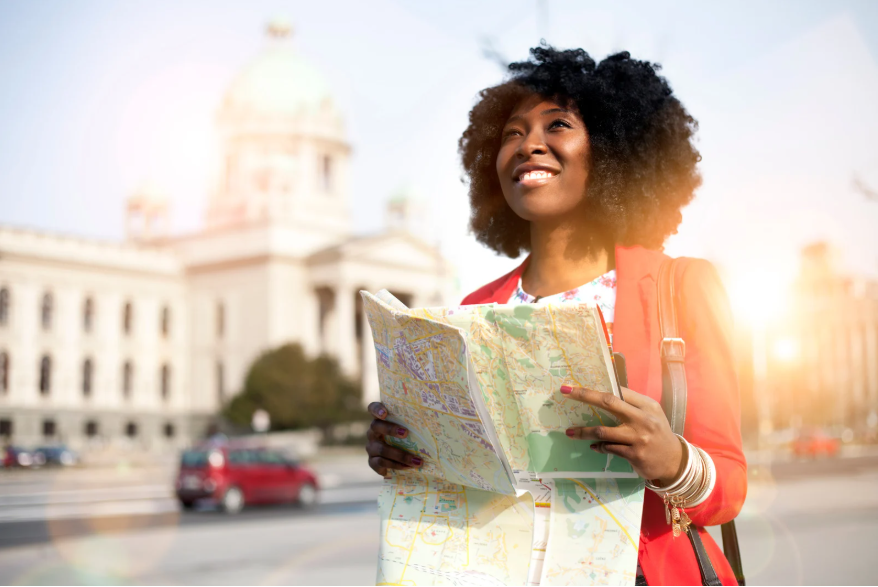Una joven que sujeta un mapa, con un monumento a su espalda.
